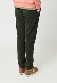 Groene corduroy broek met verticale ribbels, voorzien van zijzakken en eenRelaxte pasvorm, gecombineerd met bruinrode sneakers.