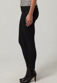 Vaqueros negros ajustados de mezclilla, con una textura suave, corte slim, tiro medio y un sutil detalle de costura. Combinados con botas de tobillo.