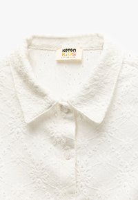Hvid skjorte med tekstureret blomsterdesign, udstyret med knaplukning og Koton Kids label, egnet til børn i alderen 6-9 år, størrelse 116-122 cm.