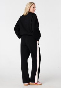 Survêtement noir à coupe ample, avec des bandes latérales roses sur le pantalon. Texture douce, taille élastique et manches larges. Agrémenté de chaussures décontractées.