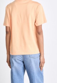  ferskenfarvet bomuld T-shirt med korte ærmer, rund halsudskæring og løs pasform, kombineret med lyseblå denimbukser. Glat tekstur og enkelt design.