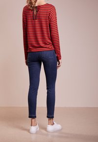 Röd och svart randig långärmad topp med detajl i ryggen, kombinerad med tajta mörkblå jeans och vita sneakers.