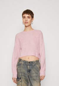 Korthalsad stickad tröja i mjuk rosa med ett texturerat mönster, rundad halsringning och långa ärmar, tillsammans med lösa, midjehöga blåjeans.