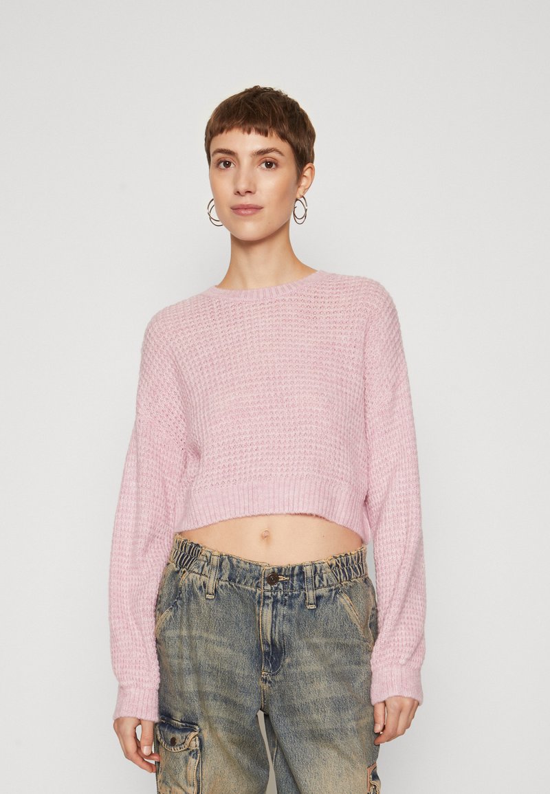 Korthalsad stickad tröja i mjuk rosa med ett texturerat mönster, rundad halsringning och långa ärmar, tillsammans med lösa, midjehöga blåjeans.