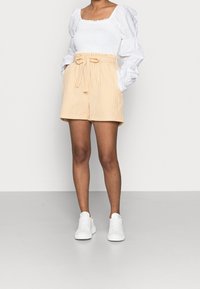 Světle žluté kostkované šortky se stahovacím elastickým pasem a zavazováním. Kombinované s bílou košilí s nadýchanými rukávy a bílými teniskami.