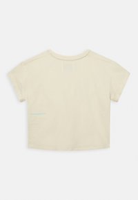 T-shirt bege de manga curta em algodão com decote redondo, apresentando um pequeno logo azul na parte traseira esquerda, perto da bainha.