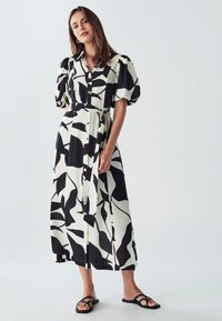 Schwarz-weißer Maxikleid mit gemustertem Design, kurzen Puffärmeln, Knöpfen auf der Vorderseite, einem Taillengürtel und einem fließenden Stoffstruktur.