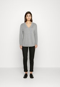 Grauer V-Ausschnitt-Pullover aus weichem Stoff mit langen Ärmeln, kombiniert mit schwarzen hochgekrempelten Hosen und schwarzen Slippern. Schlichte, legere Passform.