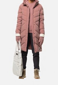 Osoba ubrana w długi różowy pikowany płaszcz, różowe rękawiczki, czarne spodnie, beżowe zimowe buty i niosąca jasnoszarą torbę na ramię.