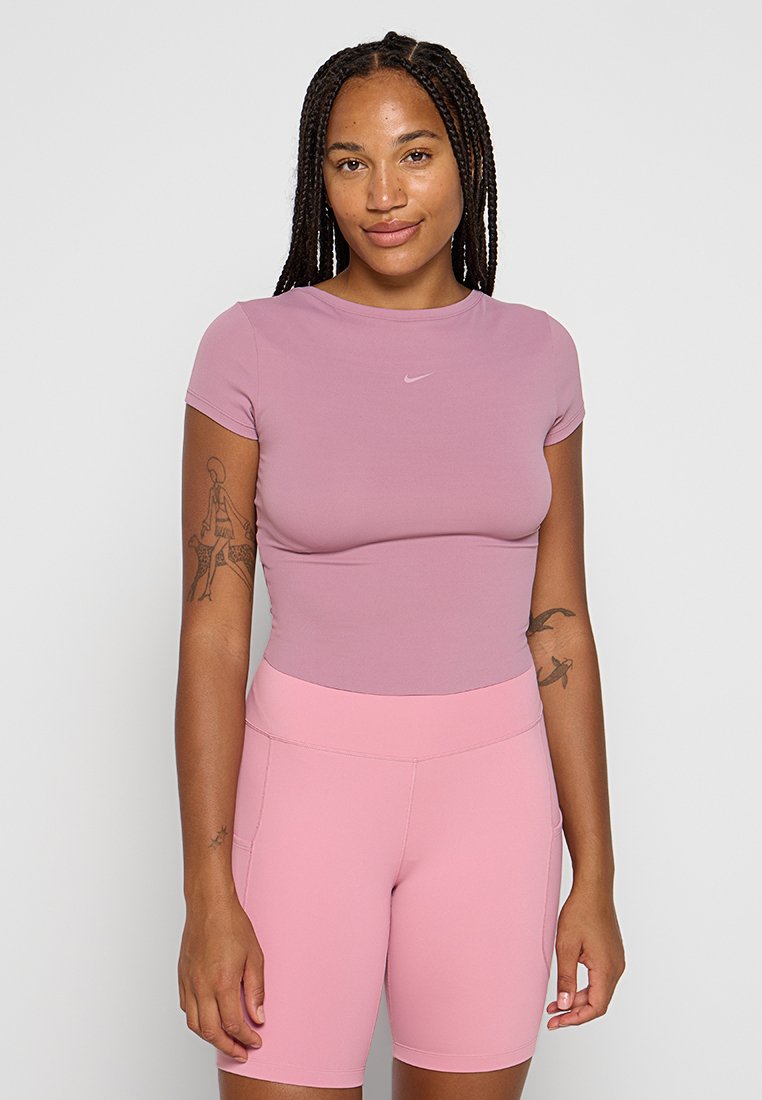 Top aderente a maniche corte di colore lilla con logo Nike; abbinato a pantaloni corti rosa elasticizzati a vita alta con tasche laterali.
