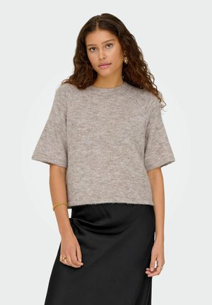 Lys pink cropped sweater med korte ærmer, lavet af blødt, tekstureret stof. Sammen med en sort satin nederdel, der skaber et lagdelt look.
