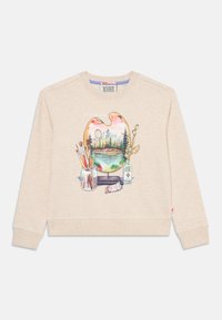 Beige Sweatshirt mit einem bedruckten Künstlerpalette, die eine Berglandschaft zeigt, Pinsel in einem Glas, eine Farbtube und getrocknete Blumen in einer Flasche.