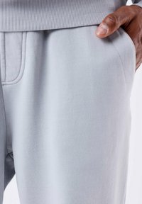 Pantalones de chándal gris claro con una cinturilla acanalada, bolsillos delanteros y una textura suave. Vista cercana centrada en los detalles del tejido y el diseño.
