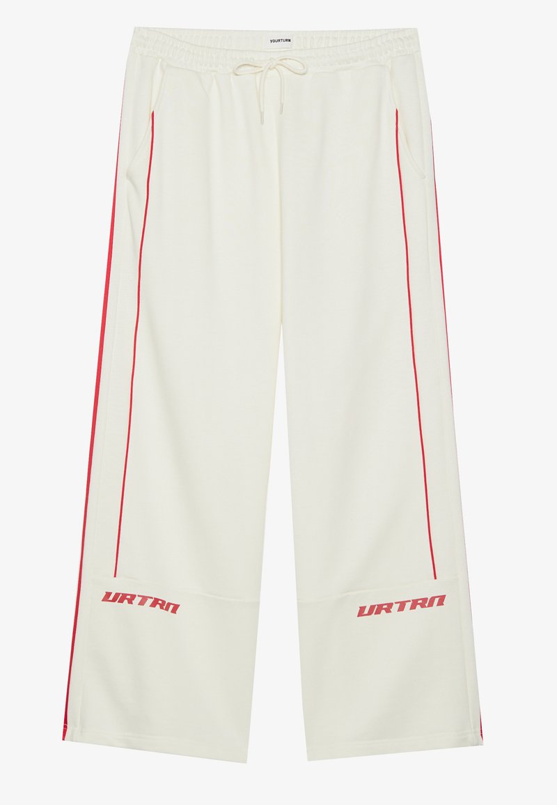 Pantalons de survêtement crème avec des rayures latérales rouges, taille élastique, cordon de serrage et logo "URTRN" sur le bas de la jambe gauche. Texture douce.