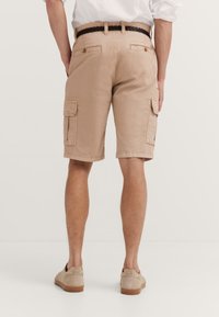 Tan cargo shorts with dual side pockets, back pockets, and a flat waistband. Made from lightweight fabric, featuring a smooth texture.