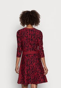 Röd och svart klänning med ett mönster av text över hela, en figursydd livdel, trekvartslånga ärmar och en utsvängd kjol.