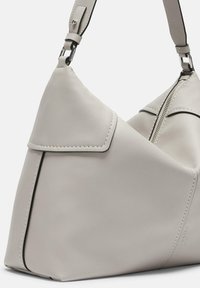 Torebka hobo w jasnoszarej skórze o gładkiej teksturze, z klapą przyskrzydlaną, kontrastowym przeszyciem i zamknięciem na zamek. Widoczny szczegół z regulowanym paskiem.