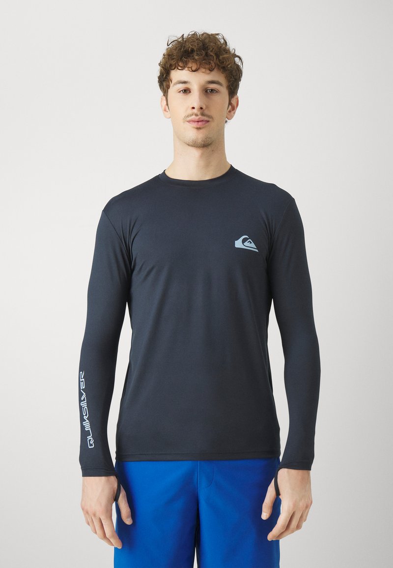 Dlhý rukáv, priliehavý čierny rash guard vyrobený z elastického materiálu, s svetlomodrým logom na hrudi a bielym textom na rukáve.
