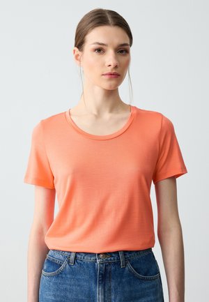 T-shirt à manches courtes de couleur corail, fabriqué en tissu lisse avec un col rond. Associé à un jean en denim bleu taille haute.