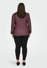 Bordeauxrode blouse met textuur en poflange mouwen, gecombineerd met zwarte skinny jeans en schoenen met blokhak, gezien van achteren.