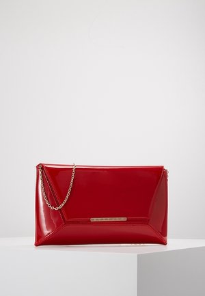 Glänzende rote Lackleder-Clutch mit dreieckiger Naht und kleinem goldenen Kettenriemen, liegend auf einer weißen Oberfläche.