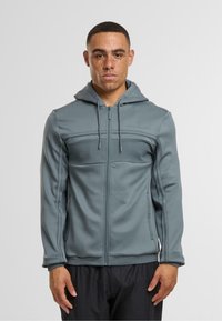 Šedá mikina na zip s texturovanou částí přes hrudník, nastavitelnou kapucí a šňůrkami; vyrobená z hladkého, pružného materiálu.