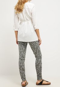 Bílá dlouhá košile s nařaseným zadním dílem a páskem v pase, zkombinovaná se šedými legínami se vzorem bílých peříček a nařasením na kotnících.