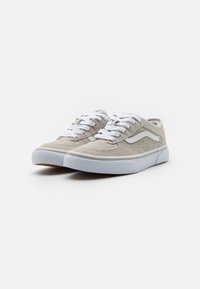 Beige suede sneakers featuring white laces and a contrasting white side stripe. The rubber sole has a toe cap and textured detailing.
