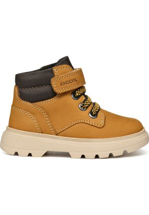 Stivale alla caviglia in pelle marrone con una fibbia in velcro, colletto scuro a contrasto, dettagli gialli sui lacci e suola beige strutturata. Visibile il marchio Geox.
