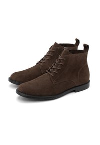 Un par de botines de ante marrón oscuro con cordones, suelas negras, cremallera lateral y bucles en la parte trasera sobre un fondo blanco.