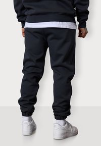 Marineblaue Sweatpants mit elastischen Bündchen und seitlichen Taschen, kombiniert mit weißen Sneakers, zeigen ein schlankes Design und eine weiche Stofftextur.