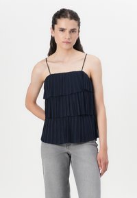 Haut plissé bleu marine avec des bretelles réglables fines ; des volants superposés créent de la texture et du mouvement. Associé à un bas en denim gris clair.
