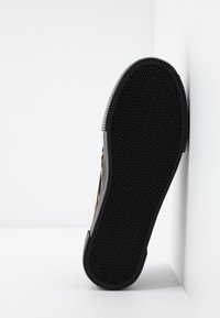 Semelle en caoutchouc noir avec motif de bande de roulement en zigzag, vue de face sur un fond d'angle blanc.