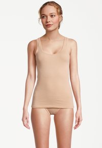 Canotta beige in tessuto liscio ed elasticizzato con spalline larghe e scollo ampio, abbinata a biancheria intima senza cuciture dello stesso colore.