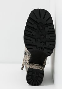 Semelle en caoutchouc noir avec un motif de crampons robuste. Tige présentant un design texturé en peau de serpent beige et noire. Détail de fermeture éclair latérale visible.