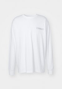 Langarm-Shirt aus weißer Baumwolle. Verfügt über ein strukturiertes graues Logo auf der linken Brustseite. Klassischer Rundhalsausschnitt und entspannte Passform.