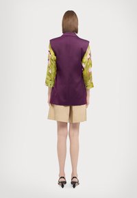 Lilla ærmeløs vest med skræddersyede skuldre, parret med gr�ønne blomsterærmer, brune shorts og sorte højhælede sandaler. Glatte stofforme.