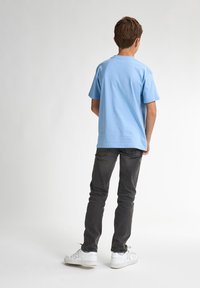 Camiseta de algodón de color azul claro con mangas cortas, de corte relajado, combinada con jeans gris oscuro y zapatillas blancas. Sin logos ni patrones visibles.