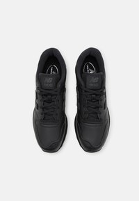 Baskets de sport noires avec tige synthétique lisse, col rembourré et lacets noirs. Dotées d'une semelle texturée et d'un logo sur la languette.