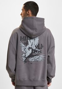 Grey oversized hoodie featuring a graphic of two doves in flight, with black text "DAYS OF OLD" on the back. Soft cotton material, relaxed fit.