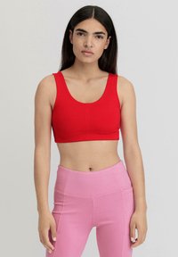 Rotes, kurzes Sport-BH mit breiten Trägern, glatter Textur und Rundhalsausschnitt. Kombiniert mit hochgeschnittenen rosa Leggings.