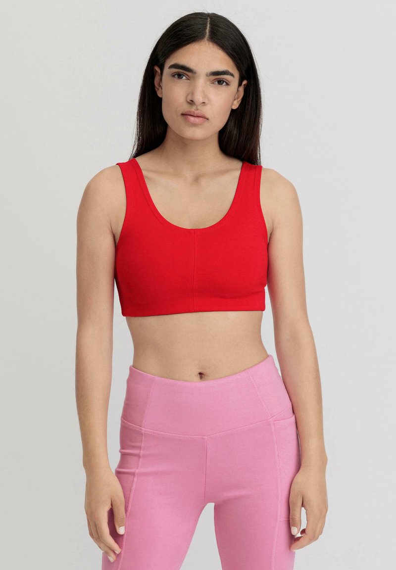 Rotes, kurzes Sport-BH mit breiten Trägern, glatter Textur und Rundhalsausschnitt. Kombiniert mit hochgeschnittenen rosa Leggings.