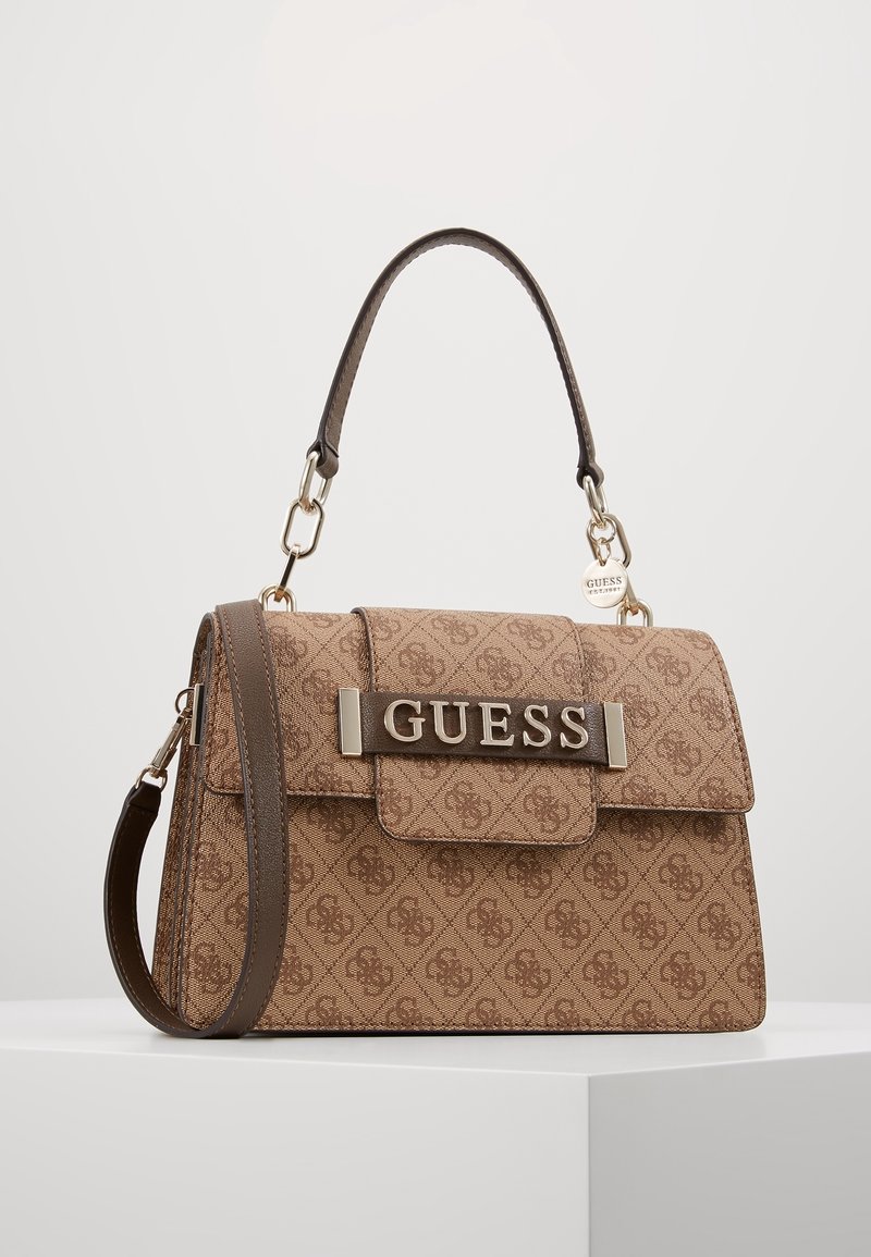 Ruskea kuvioitu käsilaukku, jossa on jämäkkä muoto, yläkahva ja irrotettava olkahihna. Etupuolella metallinen "GUESS"-logo.