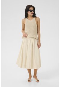 Top in maglia beige, gonna midi crema e sandali chiari. Texture morbide, vestibilità rilassata e colori solidi creano un look minimalista.