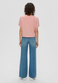 Lichtroze t-shirt met korte mouwen gecombineerd met een blauwe jeans met wijde pijpen, met een zachte textuur en een casual pasvorm. Witte schoenen maken de outfit af.