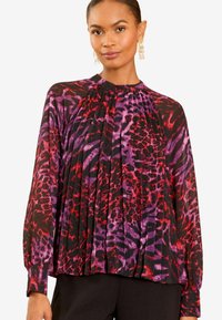 Juoda plisuota palaidinė su raudonu ir violetiniu gyvūnų raštu. Su ilgomis rankovėmis ir aukštu kaklu. Lengvas, plazdantis audinys.