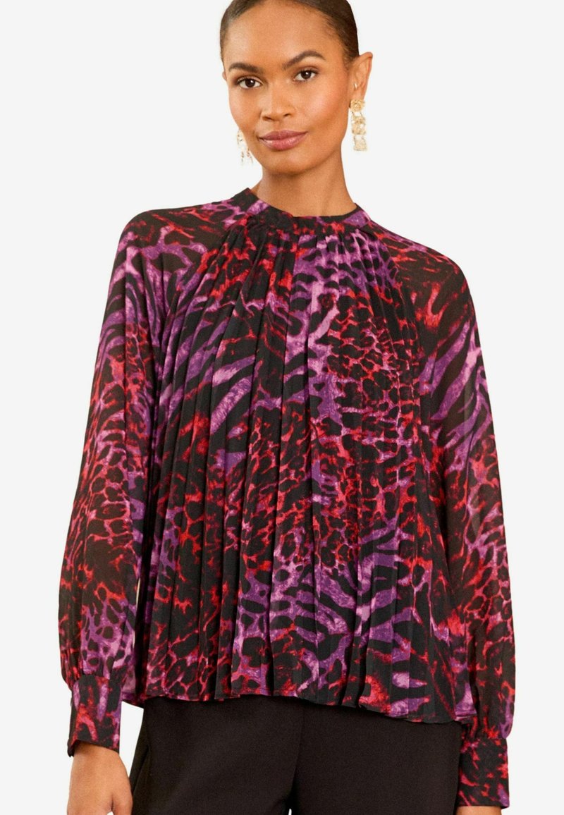 Juoda plisuota palaidinė su raudonu ir violetiniu gyvūnų raštu. Su ilgomis rankovėmis ir aukštu kaklu. Lengvas, plazdantis audinys.