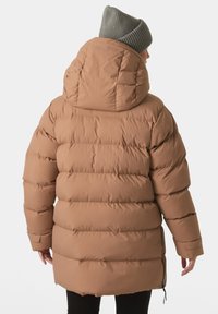 Giacca a vento marrone con cappuccio, texture trapuntata e polsini elasticizzati. Presenta una cerniera laterale e una vestibilità comoda. Berretto lavorato a maglia grigio in testa.