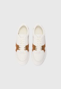 White sneaker with brown suede accents, featuring perforations, laces, and a flat sole. Smooth leather exterior and cushioned insole.