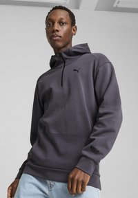 Sudadera con capucha de tela gris oscuro con media cremallera y bolsillo tipo canguro. Presenta un logo negro de Puma y puños texturizados.